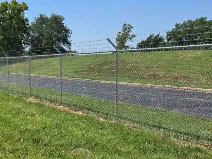 Galvanized chain link with barbed wire arms running along a road in Tulsa